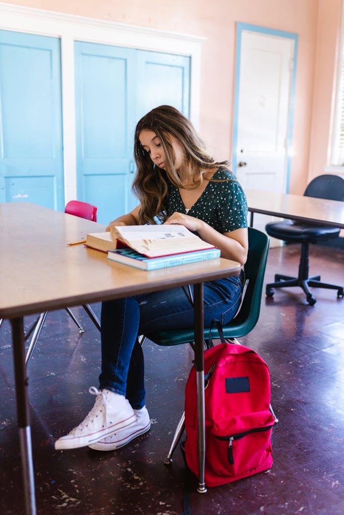 Teen girl studying in a classroom with textbooks and a vibrant red backpack.